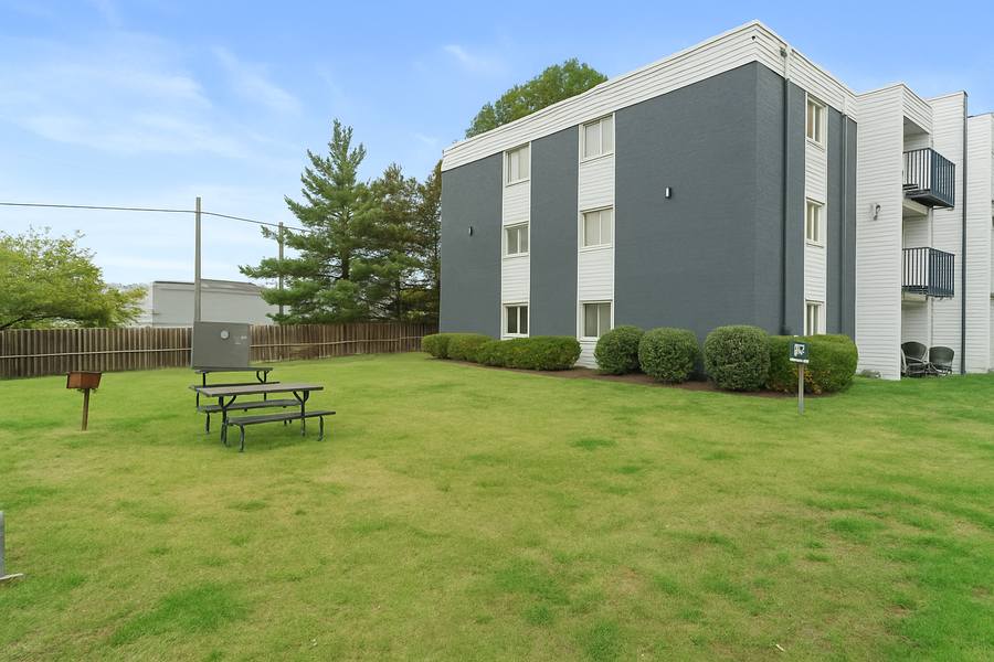 The grass lawn at the end of the building, with picnic tables and shrubs.